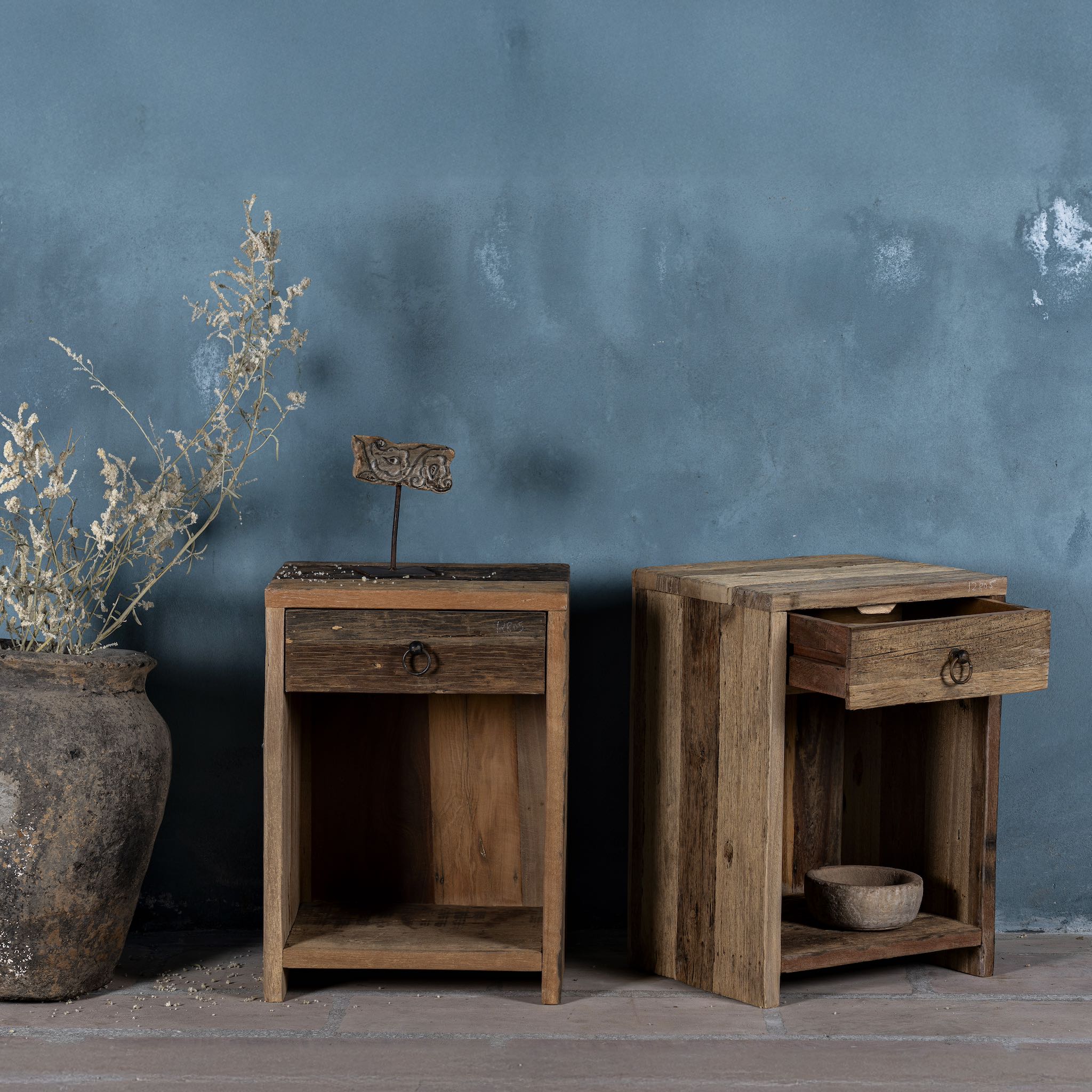 Side view image with open drawer of a pair of bedside tables in Driftwood/ Wabi Sabi style crafted from recycled old wood, each featuring a single drawer with a metal ring pull and an open shelf below, showcasing natural wood grain and rustic textures.