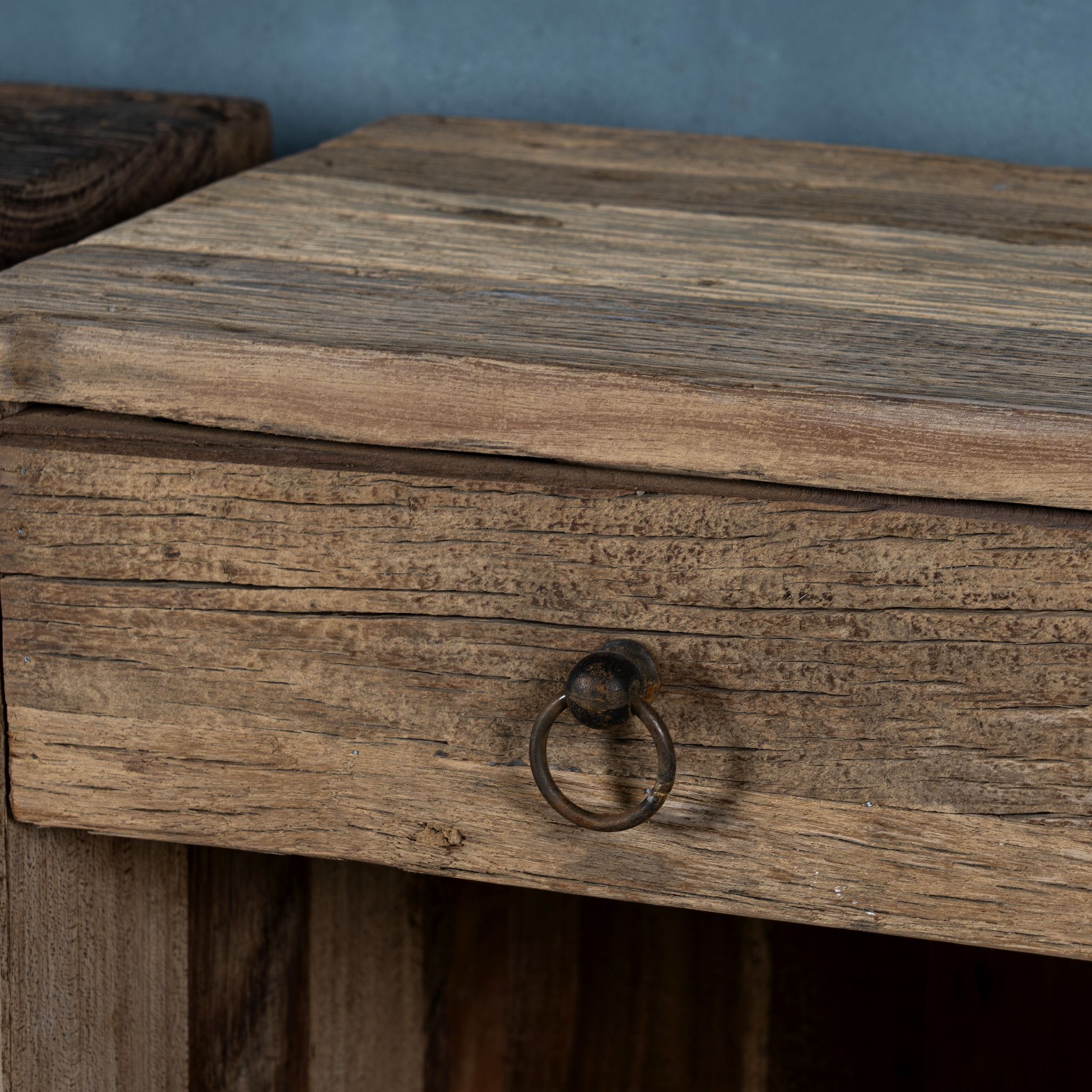 Close up image of a pair of bedside tables in Driftwood/ Wabi Sabi style crafted from recycled old wood, each featuring a single drawer with a metal ring pull and an open shelf below, showcasing natural wood grain and rustic textures.