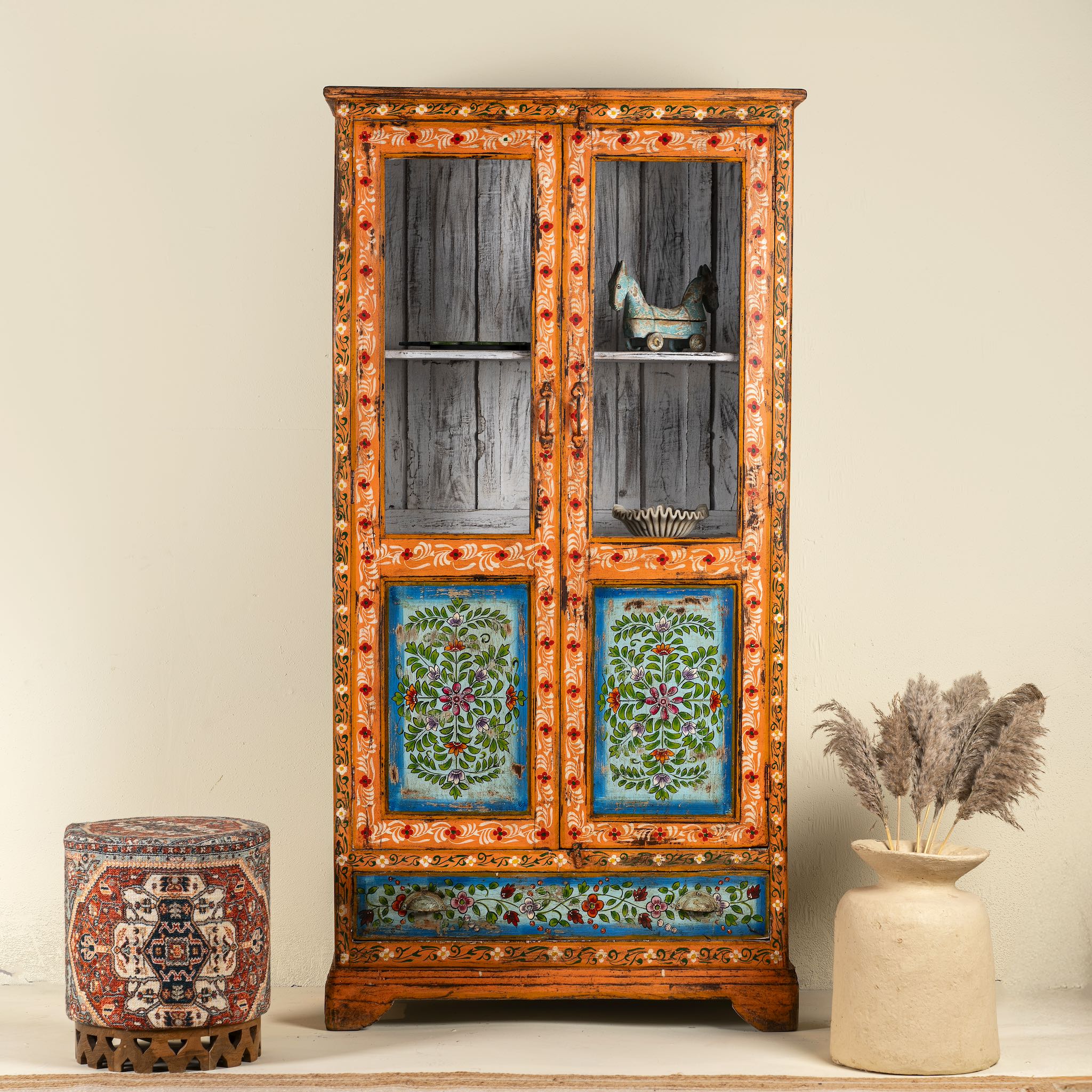 A hand-painted reclaimed wood Boho showcase with intricate floral patterns, made from refurbished teak wood, with glass doors and shelves.