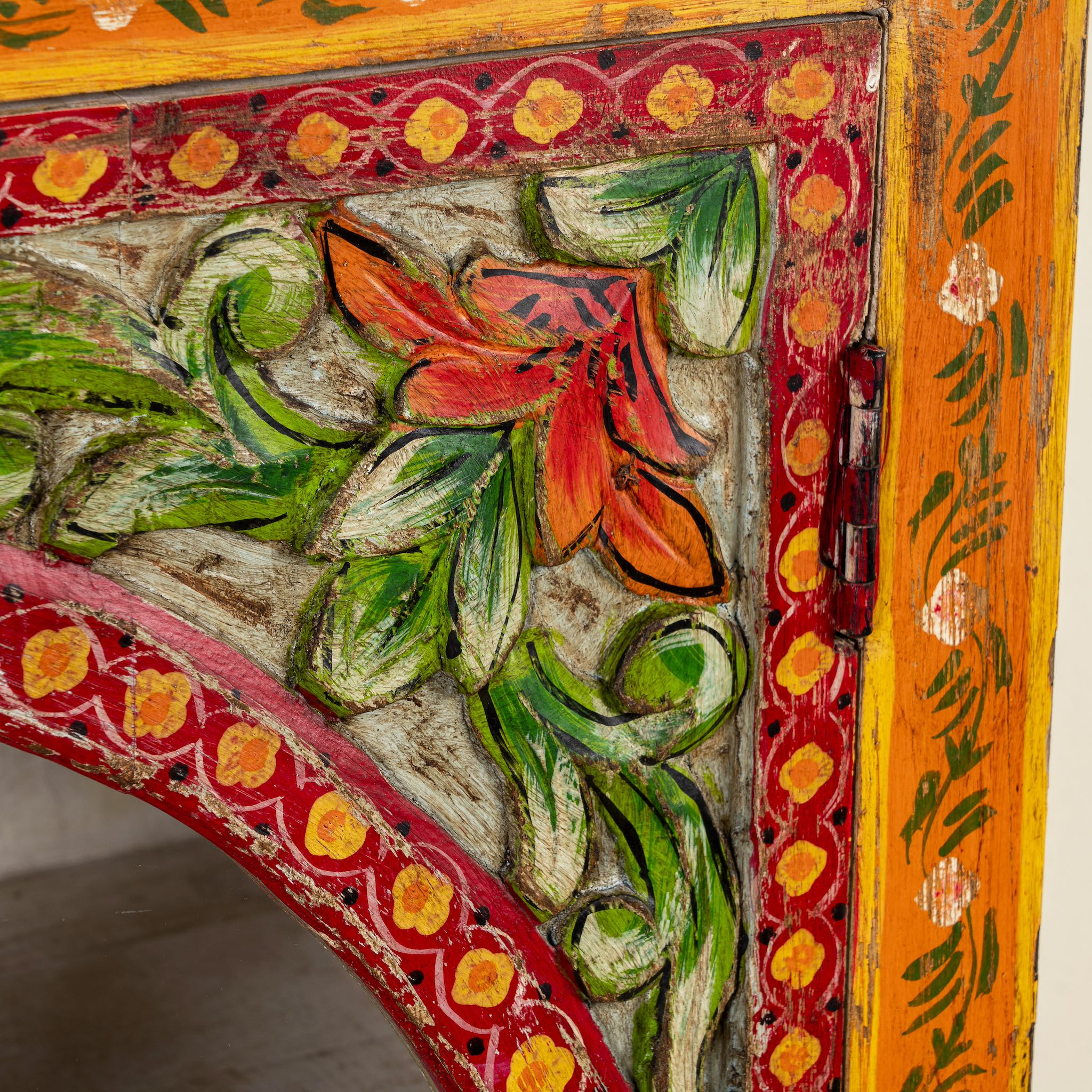Close up picture of a hand-painted showcase cabinet made from mango wood, featuring a circular glass-front display, floral motifs in rich orange, green, and red tones, and five drawers for added storage.