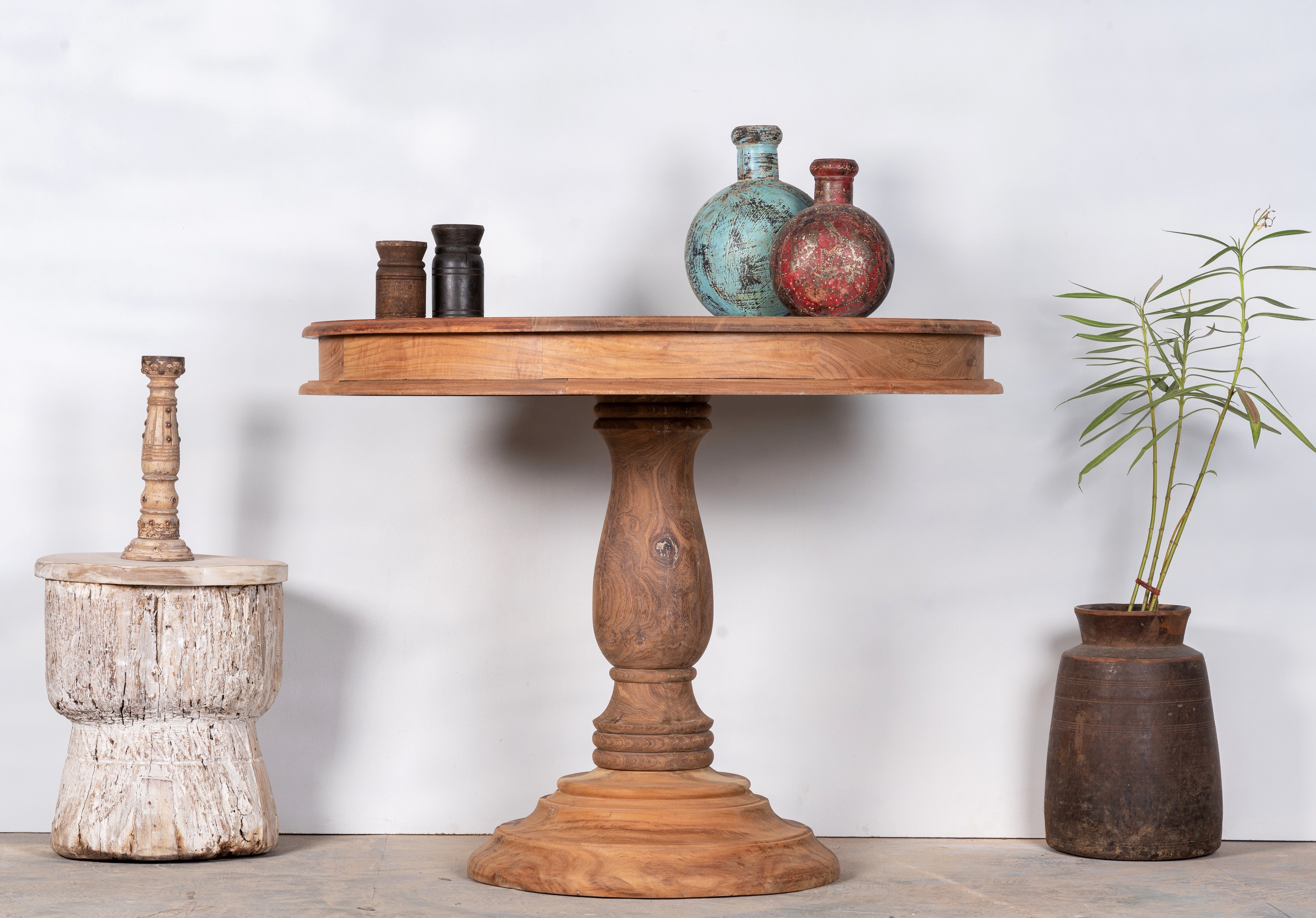 Lifestyle image of a round solid wood dining table made from reclaimed teak with carved pedestal base; rustic reclaimed teak wood dining table, 100 cm diameter × 78 cm height.
