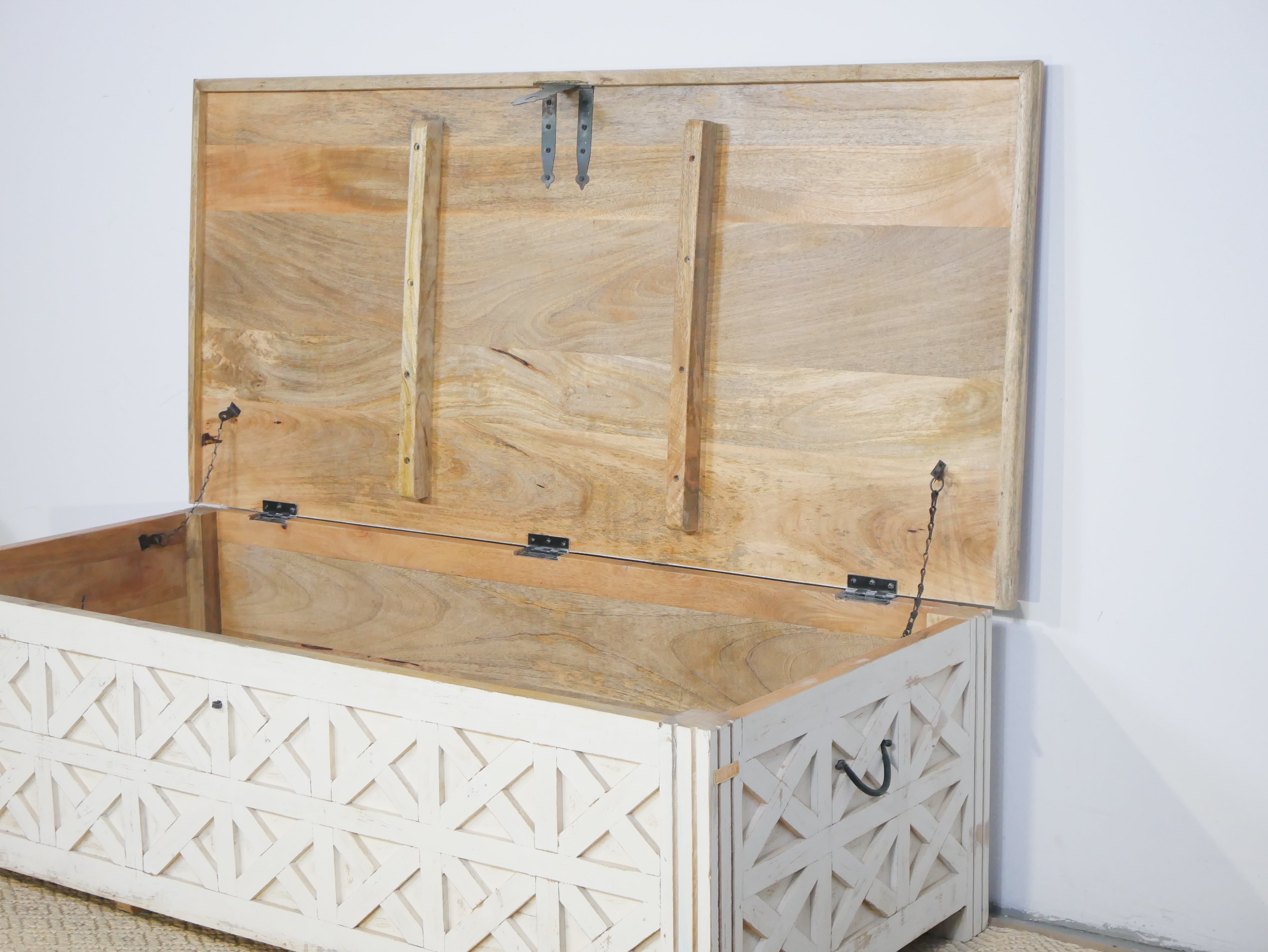 Open lid of a hand-carved mango wood vintage chest front view – styled in Mediterranean living room with books, candles, natural textures, and soft daylight.