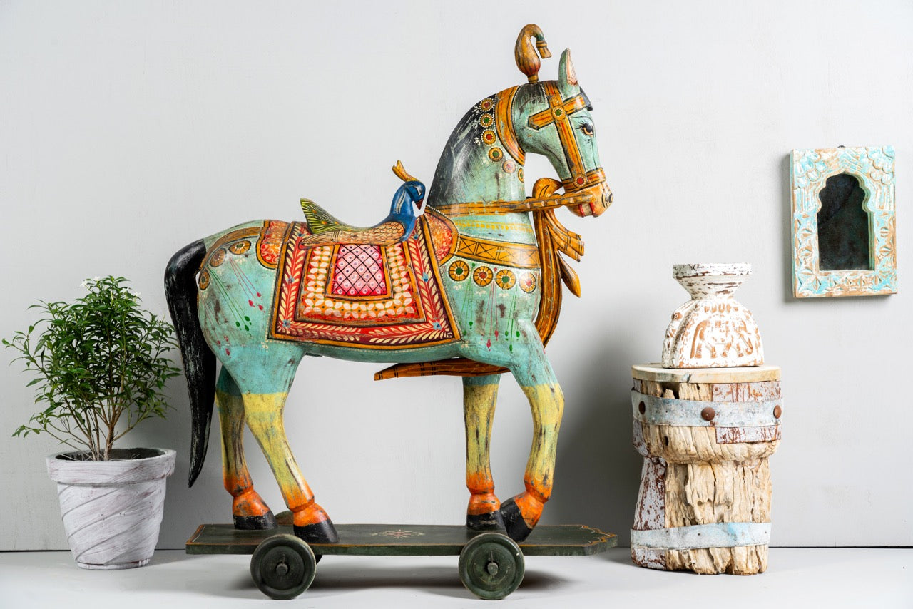 Side angle image of a large hand-painted Indian wooden horse sculpture on wheels – Rajasthani mango wood decor piece, ideal as artistic Indian home accessory, 110x90x30cm.
