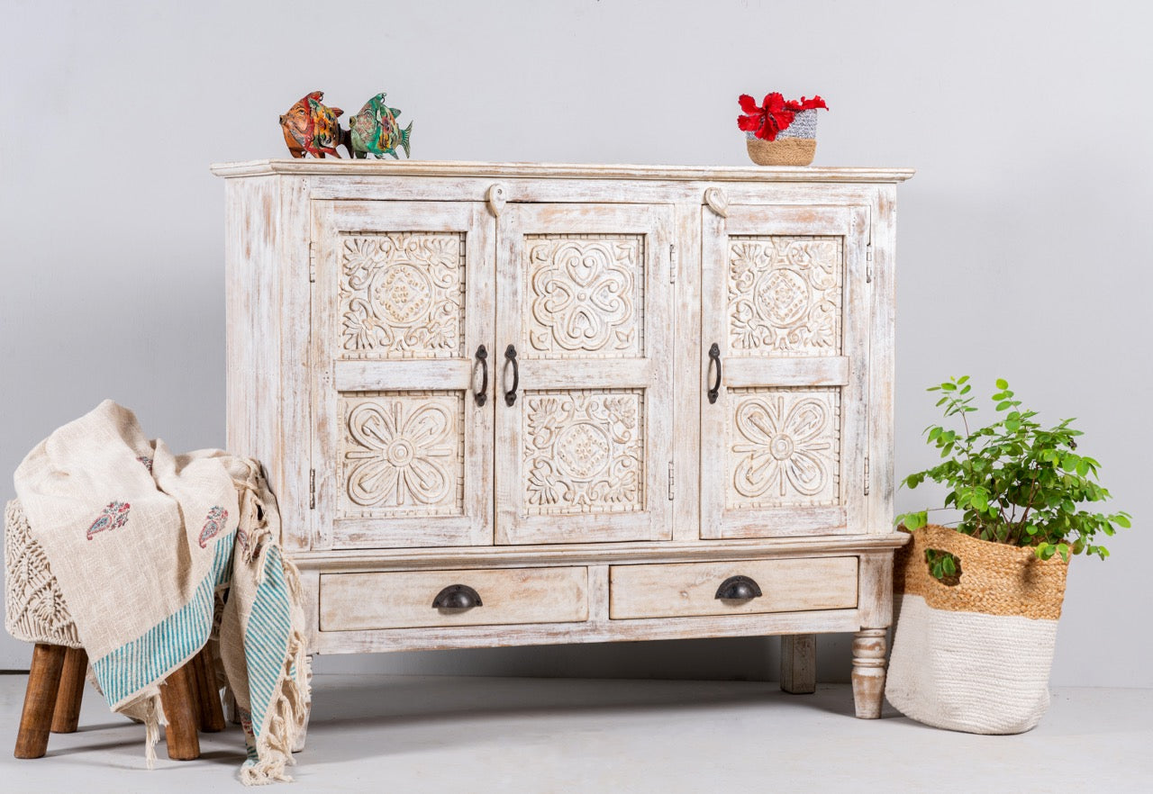 Side angle image of a whitewashed hand carved wooden sideboard made from solid mango wood with floral patterns, 3 doors and 2 drawers; artisanal mango wood furniture, 120 × 100 × 40 cm.