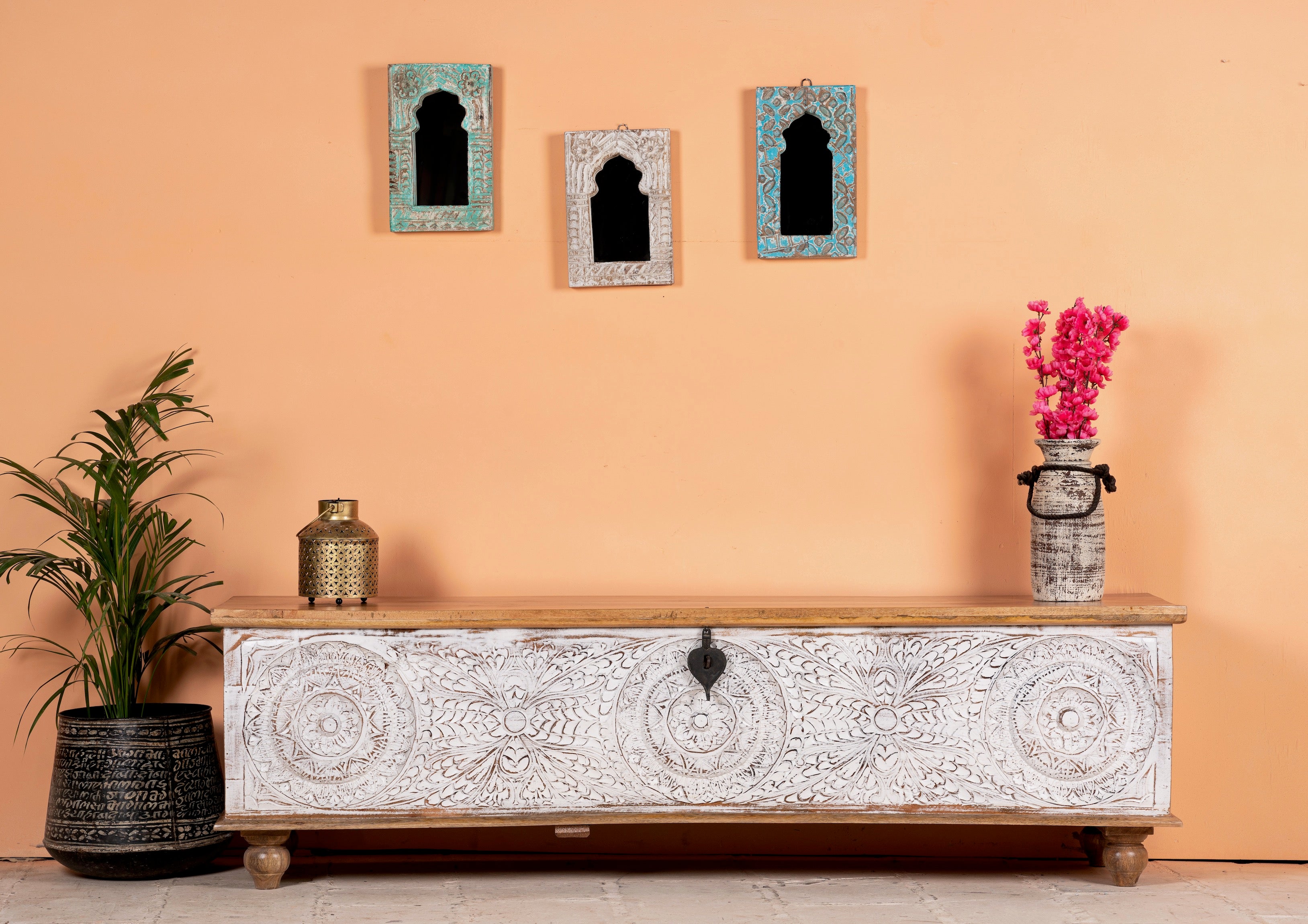 lifestyle image of a long mango wood vintage display box and wood chest box with hand‑carved circular motifs, iron fittings and whitewashed finish; 180 × 55 × 46 cm.