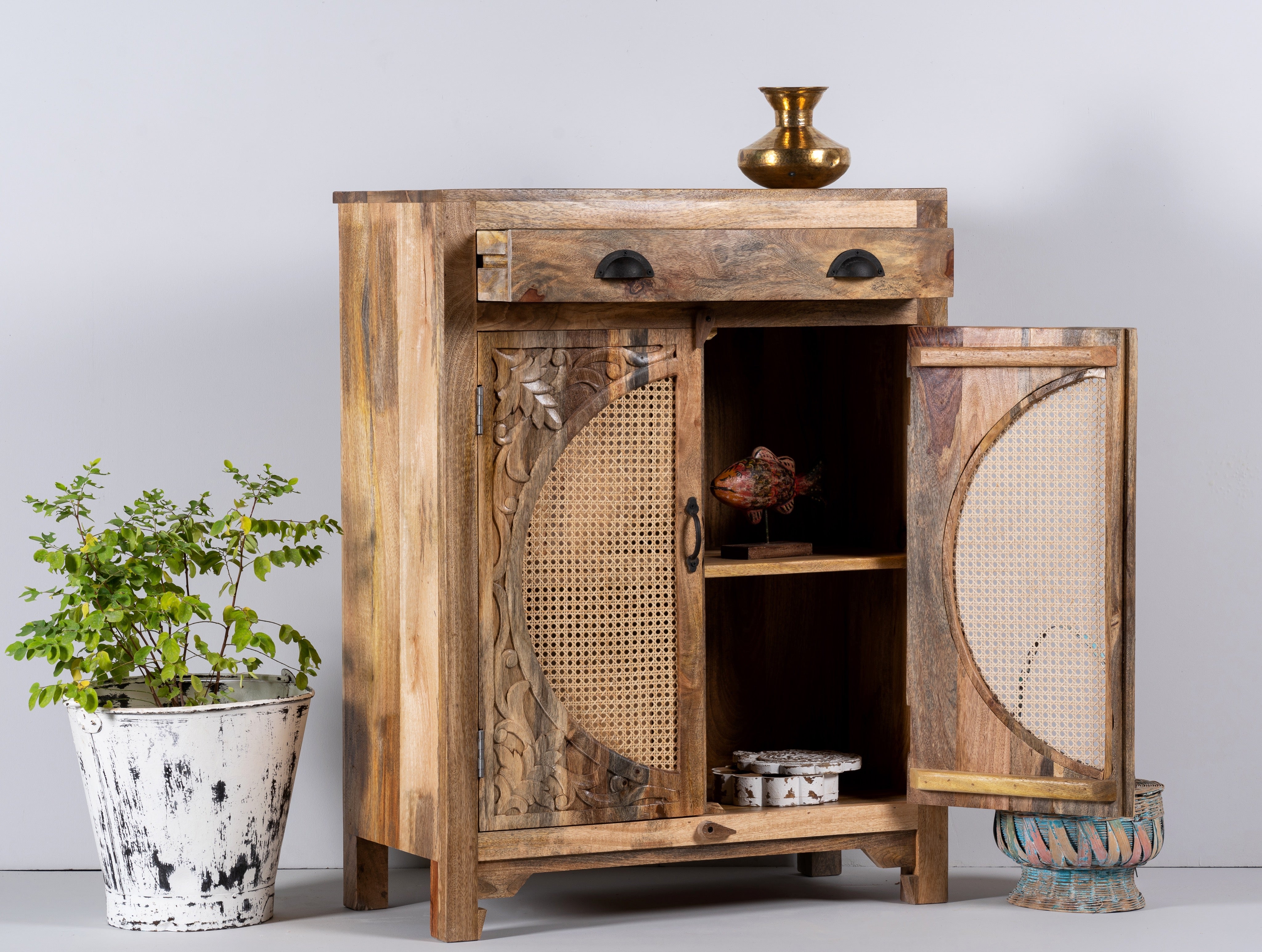 Side angle image with open doors of a mango wood cupboard with rattan door panels and hand‑carved Indian ornamentation, 80 × 40 × 104 cm.