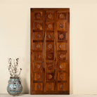 Hand-carved sliding door panel made from reclaimed wood, featuring symmetrical floral motifs in square reliefs for a warm, artisanal statement piece.