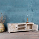 Wooden console table with intricate carvings against a textured blue wall.