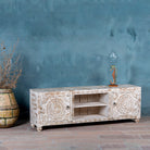 Side angle of a low board made from solid mango wood, featuring intricate hand-carved mandala motifs, whitewashed finish, and practical storage with two doors and open shelving.