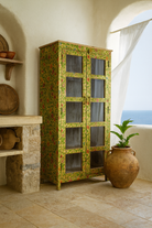 Lifestyle image of a hand-painted reclaimed wood showcase cabinet with floral motifs and glass doors, sustainable furniture and vintage home decor style, 96 × 40 × 182 cm.