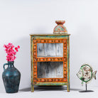 A vintage style handcrafted Indian showcase cabinet with multicolored hand-painted patterns, placed next to a vase with flowers and a decorative fish object.