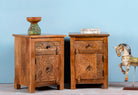 Side angle image of a pair of mango wood night stands with floral hand carvings in natural wood colour.