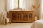 Wooden cabinet with intricate carvings in a room with a window and decorative elements.
