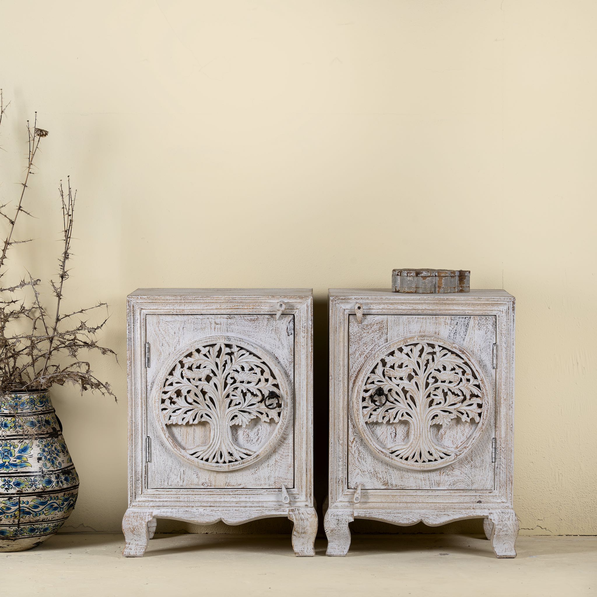 Pair of nightstands made from mango wood, featuring hand-carved tree of life designs on the doors and a whitewashed antique finish for a serene, artisanal look.