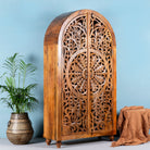 Side angle image of a half-round mango wood wardrobe with floral carvings, a unique example of sustainable furniture and artisanal furniture.