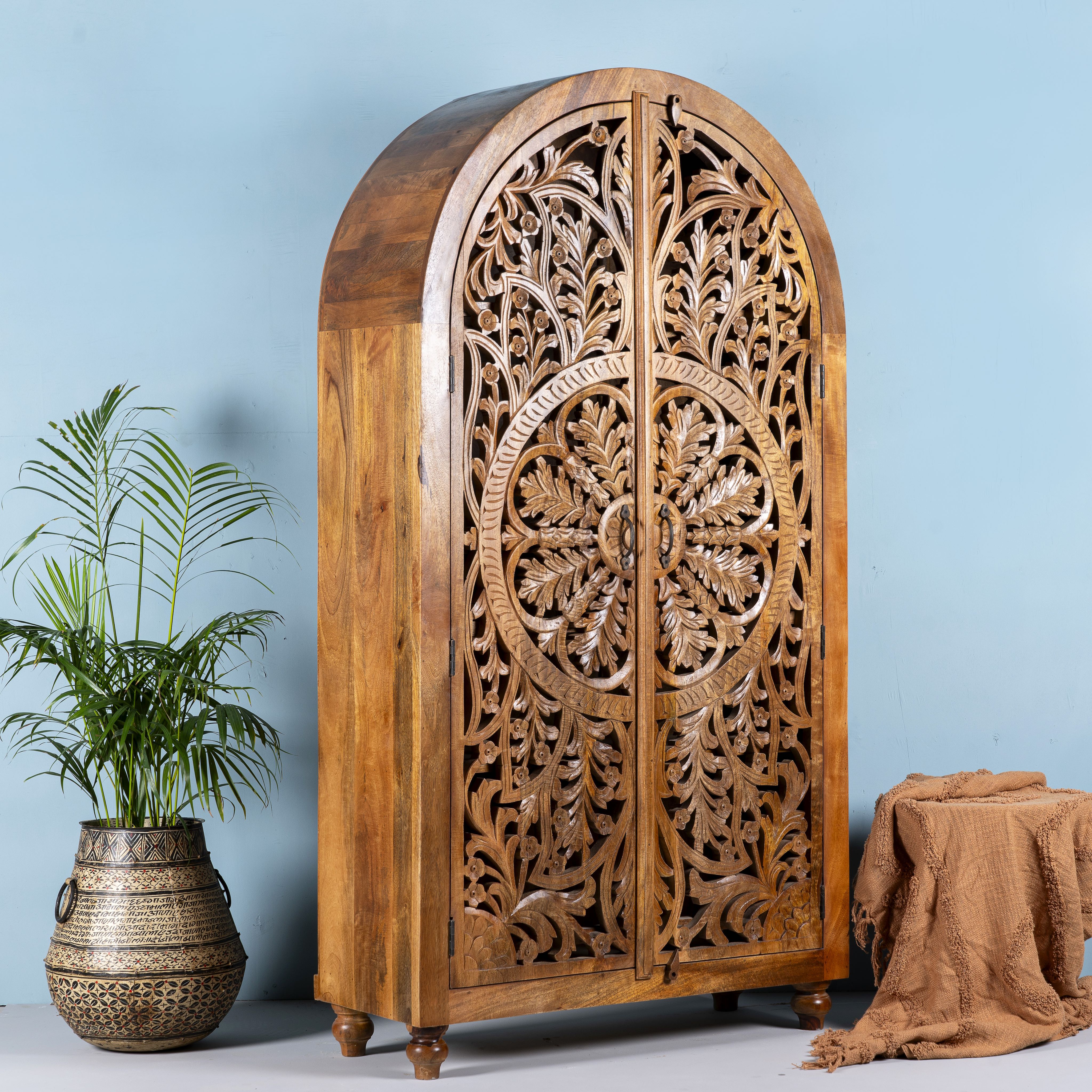 Side angle image of a half-round mango wood wardrobe with floral carvings, a unique example of sustainable furniture and artisanal furniture.