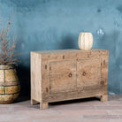 Side angle of a sideboard with hand-carved teak wood front, sandblasted for a sun-worn finish- a unique piece in rustic Ibiza style with circular mandala carvings and iron ring handles.