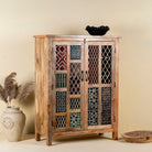 Side angle image of a artisan-made cabinet crafted from mango wood, featuring double doors adorned with a patchwork of colourful, intricately carved geometric panels, blending traditional craftsmanship with a vibrant, eclectic style.
