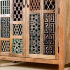 Close up side angle image of a artisan-made cabinet crafted from mango wood, featuring double doors adorned with a patchwork of colourful, intricately carved geometric panels, blending traditional craftsmanship with a vibrant, eclectic style.
