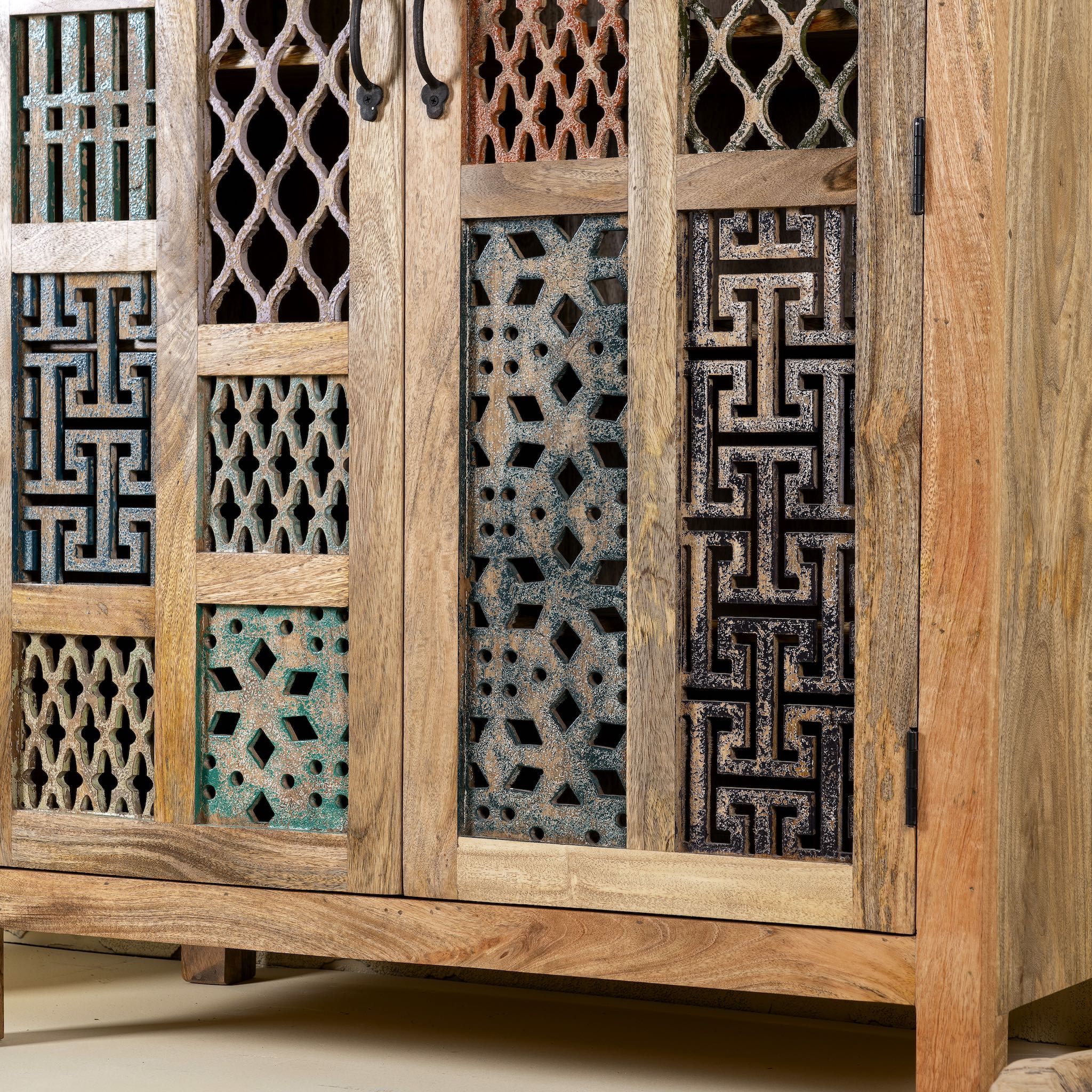 Close up side angle image of a artisan-made cabinet crafted from mango wood, featuring double doors adorned with a patchwork of colourful, intricately carved geometric panels, blending traditional craftsmanship with a vibrant, eclectic style.
