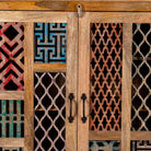 Close up image of a artisan-made cabinet crafted from mango wood, featuring double doors adorned with a patchwork of colourful, intricately carved geometric panels, blending traditional craftsmanship with a vibrant, eclectic style.

