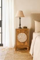 Lifestyle scene wirt a whitewashed mango wood nightstand with hand-carved floral door – a handcrafted example of carved wooden furniture ideal for rustic and vintage bedrooms.
