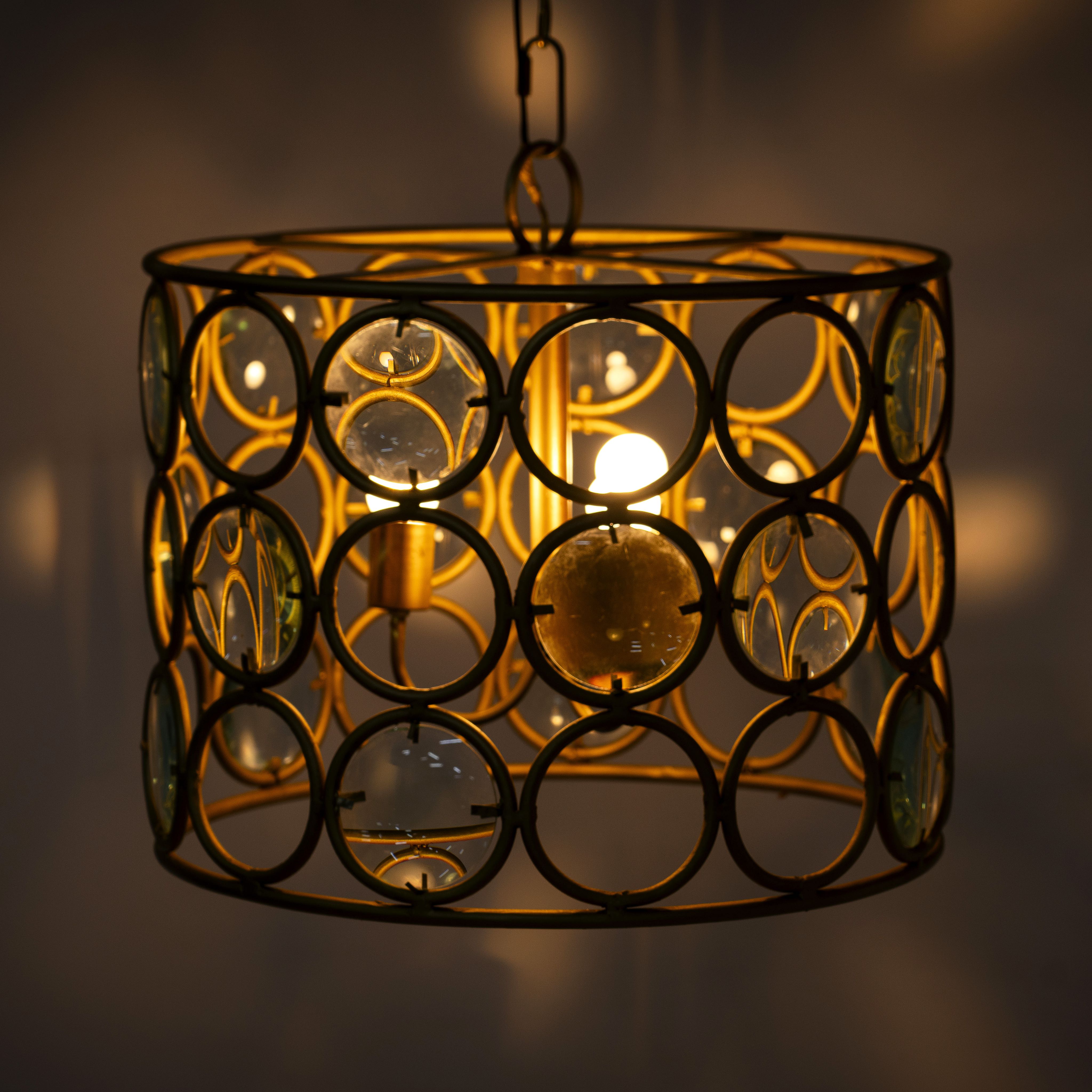 Image with a lighted round unique pendant light with shiny brass-plated iron frame and magnifying glass inserts – vintage lighting with elegant three-light design for kitchens, dining areas, or living rooms.