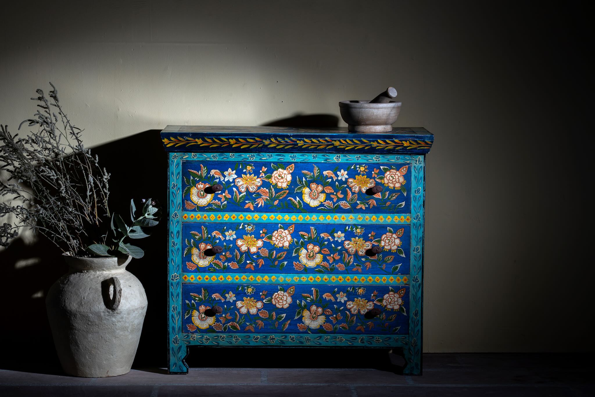 Lifestyle image of a hand-painted cupboard made of reclaimed wood with floral drawer fronts – Divisha model by Om Home & Garden