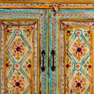 Close up image of a hand-painted sideboard made from reclaimed wood, featuring four intricately detailed doors with vibrant floral and geometric motifs in soft blues, yellows, and reds, finished with a distressed vintage patina for a charming, artisanal look.
