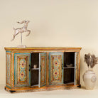 Side angle image with open doors of a hand-painted sideboard made from reclaimed wood, featuring four intricately detailed doors with vibrant floral and geometric motifs in soft blues, yellows, and reds, finished with a distressed vintage patina for a charming, artisanal look.
