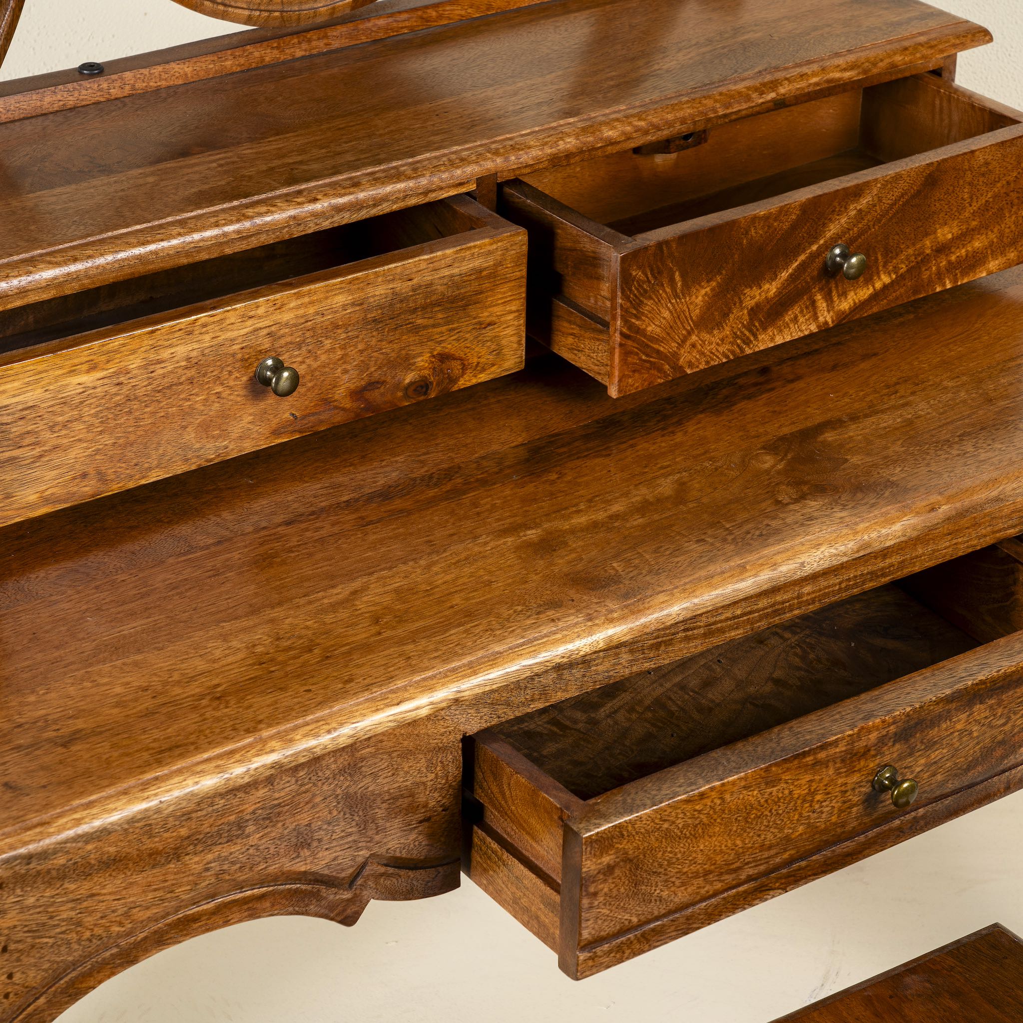 Close up image of a handcrafted mango wood cosmetic table with a curved mirror and a matching chair.