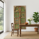 Lifestyle image of a Gitra hand-painted teak door panel featuring floral motifs in soft pastels and a carved arched frame—an elegant and unique Indian wall decoration repurposed from antique architecture.