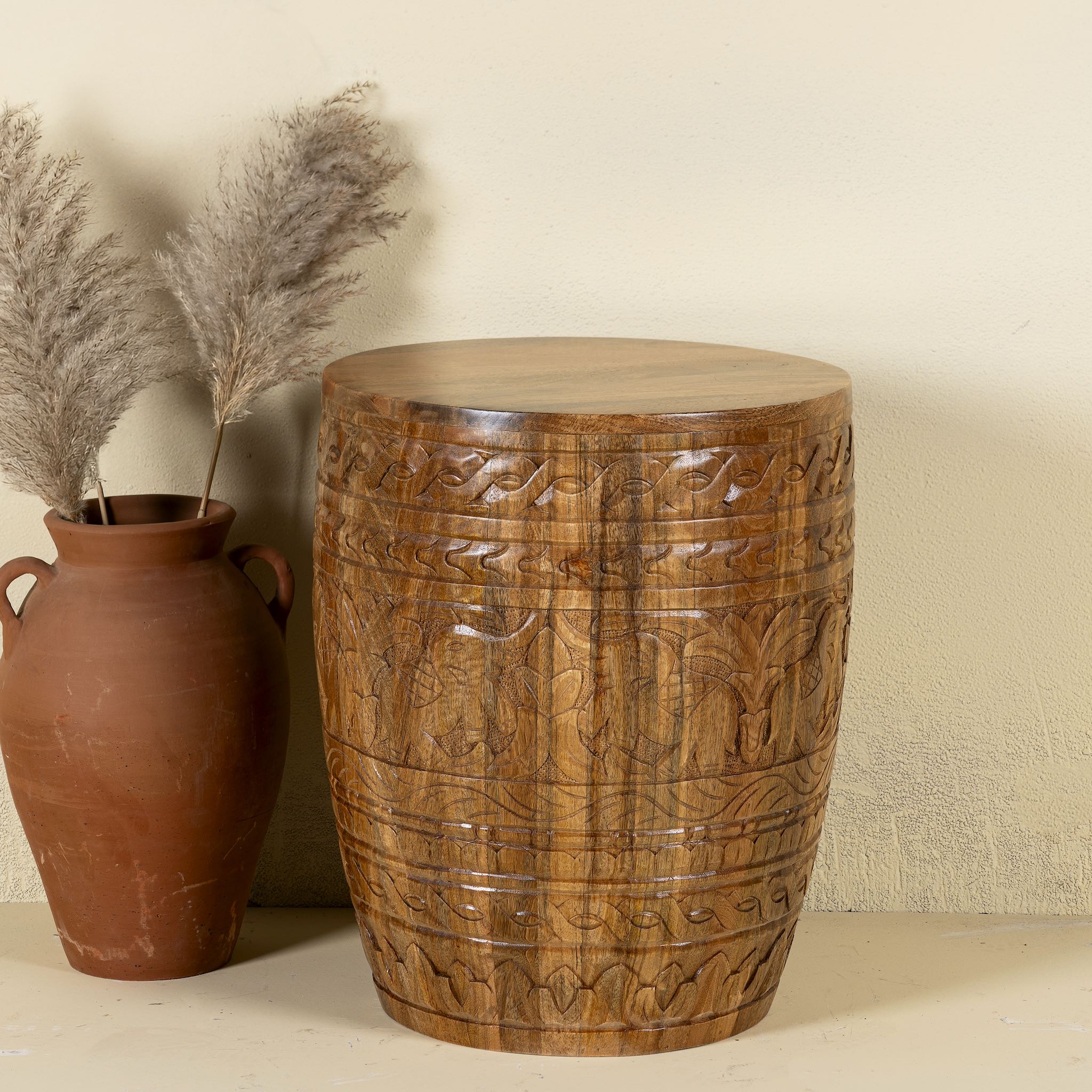 Front view of a round barrel design mango wood side table with hand carved floral designs.