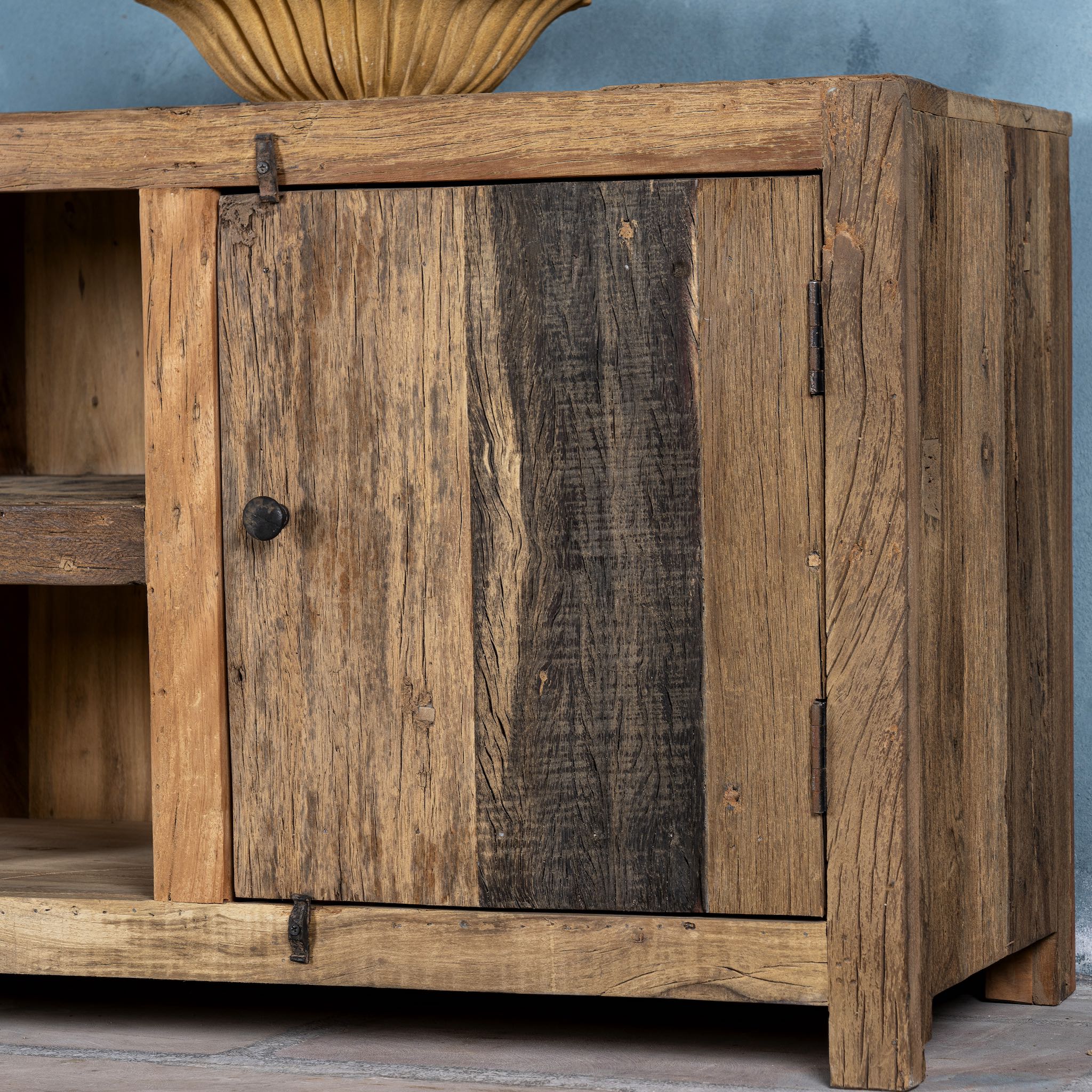 Close up image of a rustic sideboard in Driftwood/Wabi Sabi style made from recycled old wood, featuring a natural, weathered finish with two cabinet doors and open central shelving.



