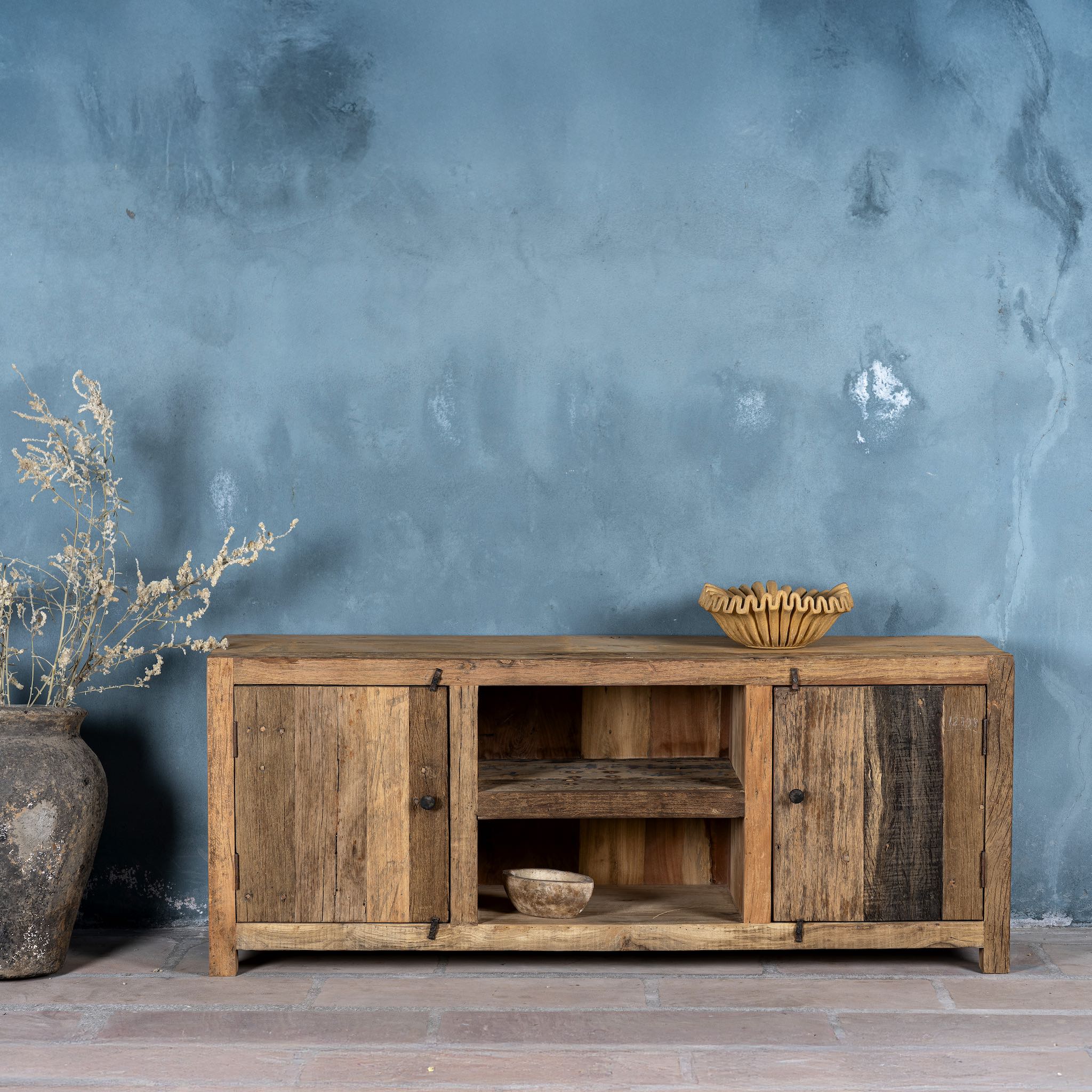 Front view of a rustic sideboard in Driftwood/Wabi Sabi style made from recycled old wood, featuring a natural, weathered finish with two cabinet doors and open central shelving.


