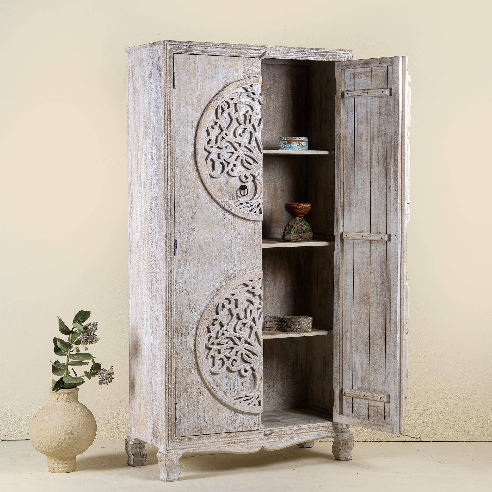 Open door image of a whitewashed mango wood wardrobe featuring intricate hand-carved double tree of life design on the doors.
