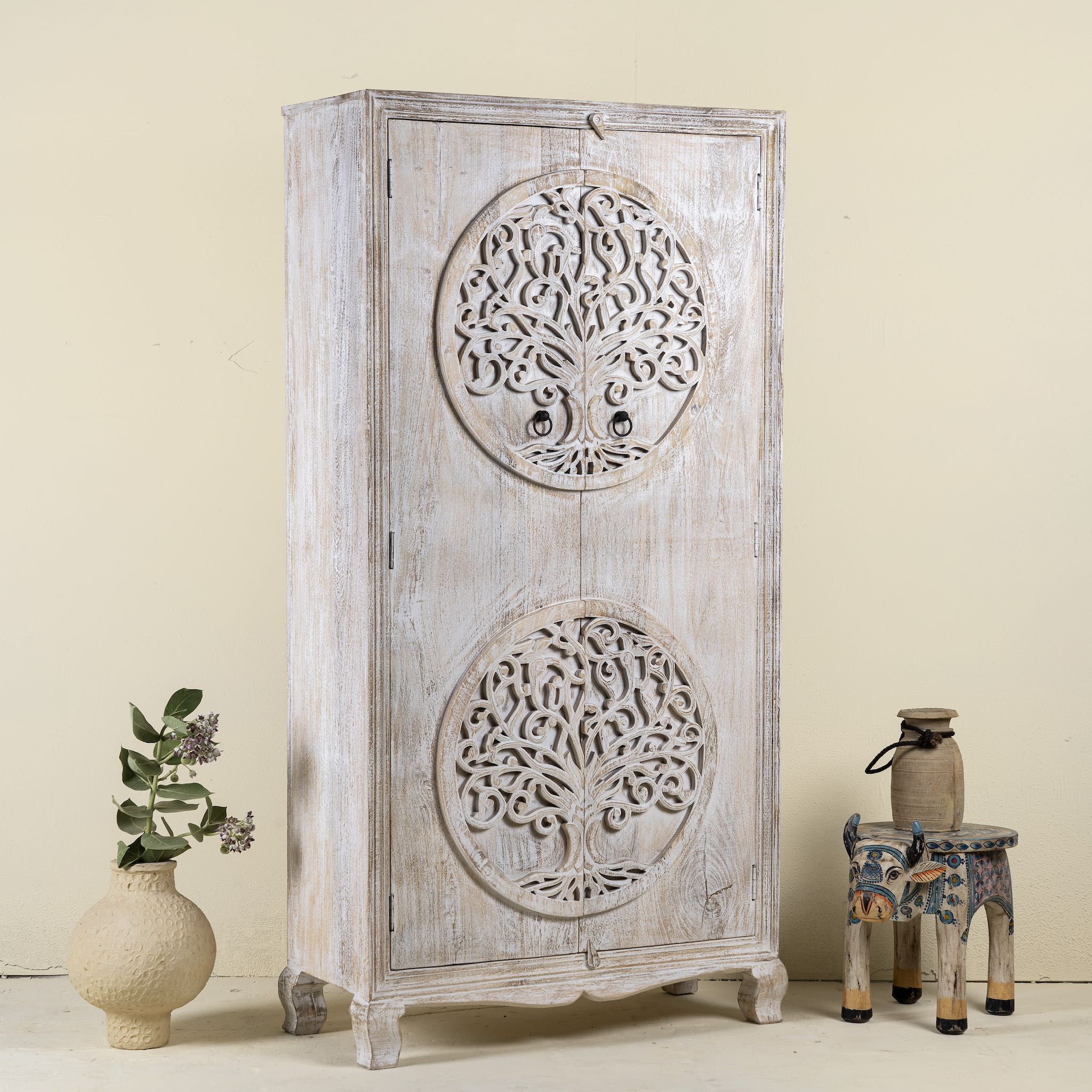 Side view image of a whitewashed mango wood wardrobe featuring intricate hand-carved double tree of life design on the doors.
