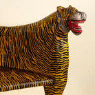 Close up image of the head of a bold hand-painted bench made from reclaimed wood, designed with double tiger heads at each end and a vibrant yellow-and-black striped pattern throughout, combining whimsical animal form with striking folk-art flair.
