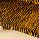 Close up image of a bold hand-painted bench made from reclaimed wood, designed with double tiger heads at each end and a vibrant yellow-and-black striped pattern throughout, combining whimsical animal form with striking folk-art flair.
