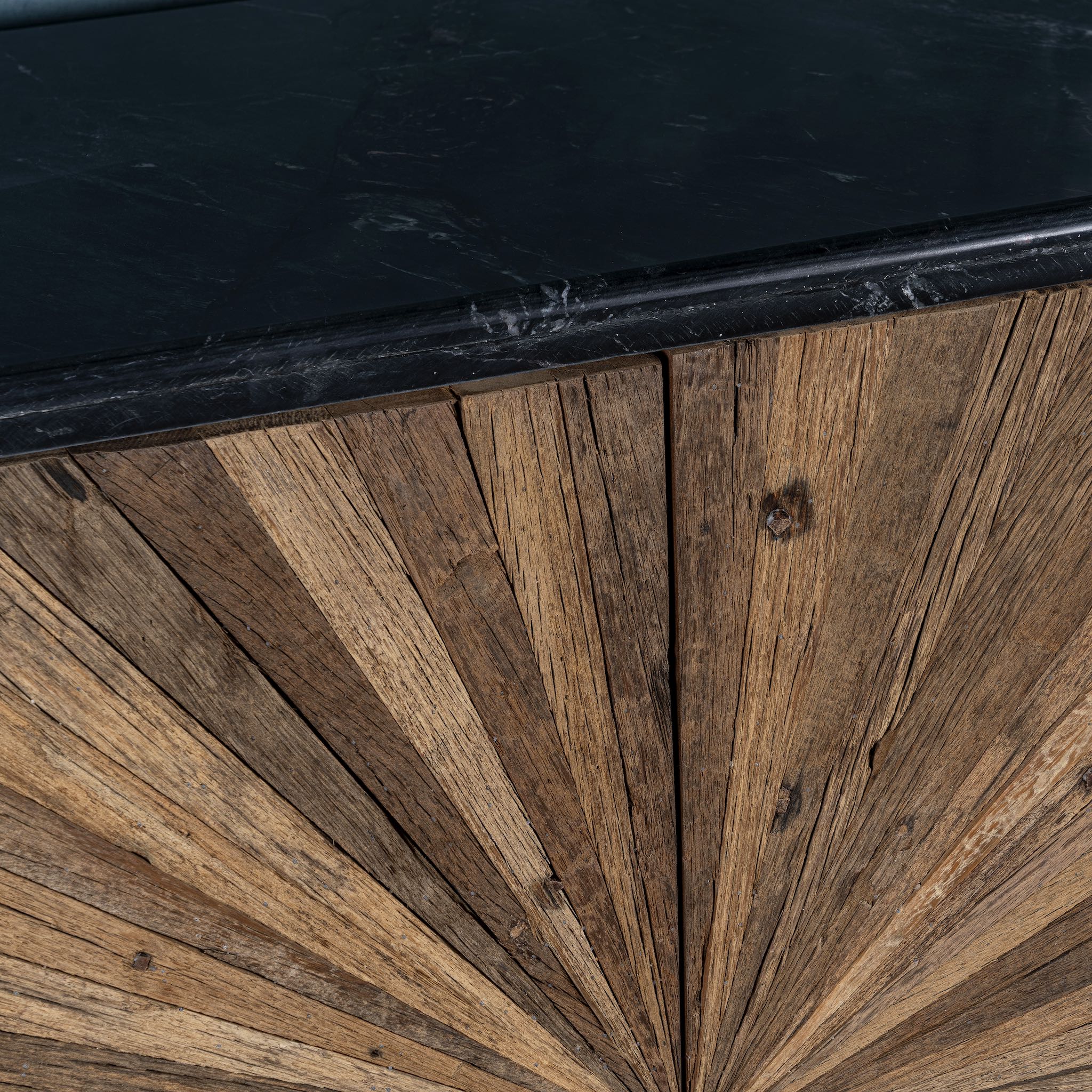 Close up of the marble top of a rustic-style cabinet made from reclaimed wood, featuring a striking sunburst pattern on the double doors, round metal pulls, and a contrasting black marble top that adds a refined touch to its natural, weathered look.
