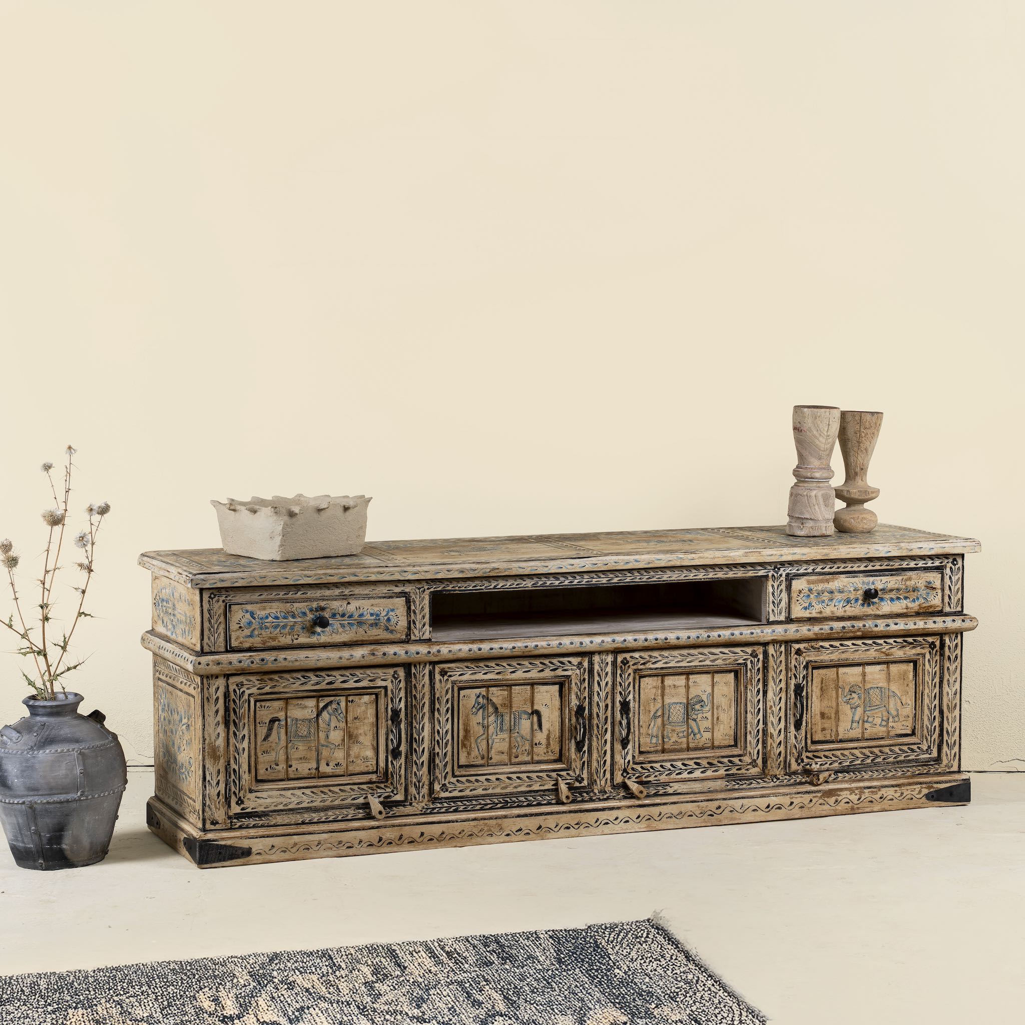 Side angle image of a hand-painted lowboard made of reclaimed wood with traditional Indian animal motifs, featuring drawers and cabinets for storage, rustic finish, and artisanal detailing.
