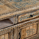 Close up image of a hand-painted lowboard made of reclaimed wood with traditional Indian animal motifs, featuring drawers and cabinets for storage, rustic finish, and artisanal detailing.
