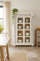 Lifestyle image of a handcrafted mango wood cabinet with glass-panelled doors and internal storage – carved wood furniture made from sustainable mango wood with unique natural grain.