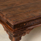 Close-up of a wooden table with intricate carvings and metal studs.