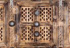 Close up image of an antique Indian treasure chest in solid teak with sandblasted finish, hand-carved details, and iron accents. Vintage home accessory for eclectic Indian decor, 127 × 110 × 47 cm.