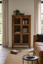 Lifestyle image of a compact reclaimed teak wood display cabinet with two glass doors and shelving – sustainable teak wood furniture combining functional design and unique character.