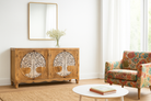 Lifestyle image of a hand-carved mango wood sideboard with Tree of Life motif, whitewashed finish, and four storage compartments; artisanal mango wood furniture for dining rooms, entryways, or living areas, 180 × 90 × 40 cm.