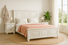 Lifestyle inspiration of a whitewashed mango wood bed frame with carved panel design and two matching nightstands; rustic bedroom furniture set, bed size 180×200×140 cm, nightstands 50×40×65 cm.