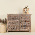Front view image of a hand-carved sideboard made from mango wood, featuring intricate geometric and floral patterns across the drawers and cabinet door, with a distressed whitewashed finish that enhances its vintage artisanal appeal.
