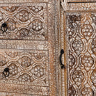 Close up image of a hand-carved sideboard made from mango wood, featuring intricate geometric and floral patterns across the drawers and cabinet door, with a distressed whitewashed finish that enhances its vintage artisanal appeal.
